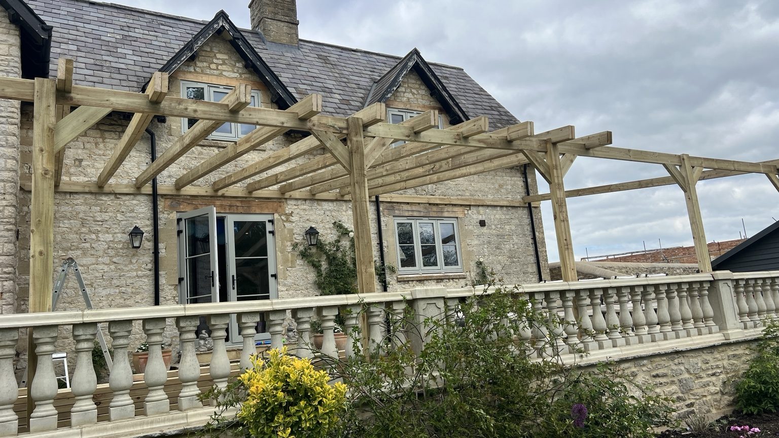 Timber pergola beside a stone house